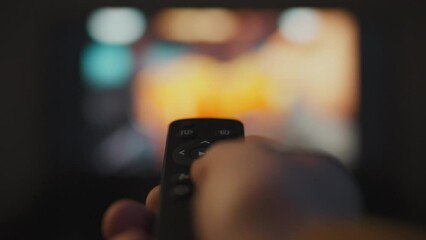 Evening relaxation of a young modern man watching television channels on the sofa using the TV remote control. The TV is controlled in a home theater. Pressing buttons switches channels