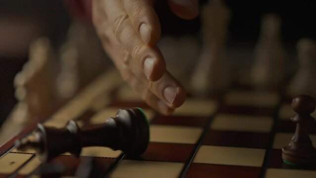 Overthrow of the king chess piece. A young experienced player knocks over a chess piece onto the board demonstrating victory. Close-up of a chess player's hand knocking over a king piece