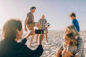 Multigenerational family having fun playing soccer on the beach