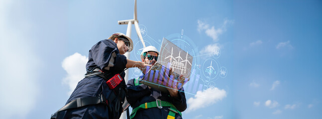 Team of engineers working on site in wind turbine farm with clear blue sky on the background....
