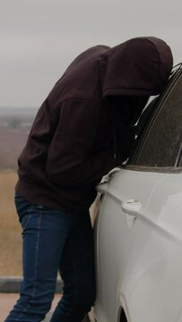 Shadowy figure hooded jacket covertly attempts break parked car intending steal vertical video. Prevalence car thefts urban areas evoking concern vehicle security steal car criminal activities.