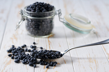 metal spoon with raw black beans on a light table, selective focus.