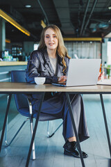 Young executive woman sitting at a desk with a cup of coffee and a laptop while working in the office.