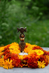 Triple Goddess figurine with candle and colorful flowers in garden, nature background. Symbol of...