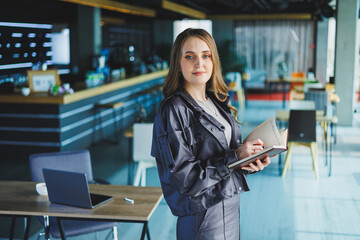 A young woman in the office makes notes in a notebook. A business woman works in a modern workspace