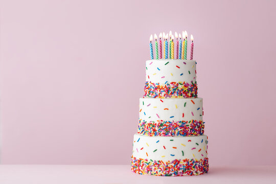 Tiered birthday cake with colorful sprinkles and birthday candles