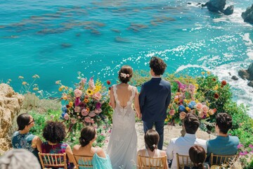 Newlywed couple holding hands by the ocean after their wedding, surrounded by colorful flowers and guests with a breathtaking cliffside view in the background - Powered by Adobe