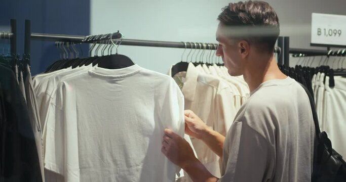 Men's clothing store caucasian mid adult man browses racks garments choices person select clothes men's fashion. Millennial male clothing shop choosing clothes men's clothing shopping mall wardrobe.