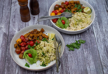 Vegan  pasta bowls- seitan cubes, vegan pesto and macaroni, roasted cherry tomatoes.  Wooden table, copy space.