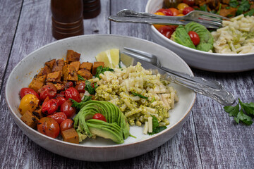 Vegan  pasta bowls- seitan cubes, vegan pesto and macaroni, roasted cherry tomatoes.  Wooden table, copy space.