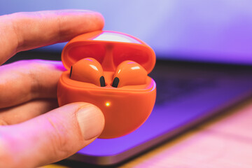 Box with Orange Wireless Bluetooth Earphones in man's hands. Modern Stereo Headphones, Sports...