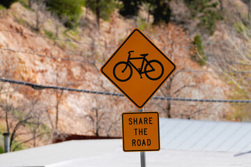 Share the Road yellow bike sign on sunny day with roof and power lines in background. 