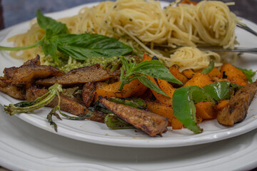 Vegan pasta bowl with seitan and roasted veggies. White plate, stylish survace