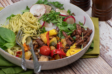 Vegan pasta bowl with seitan and roasted veggies. White plate, stylish survace