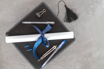 A black graduation cap, a rolled-up diploma with a blue ribbon, pencils, pens, a stapler, a phone...