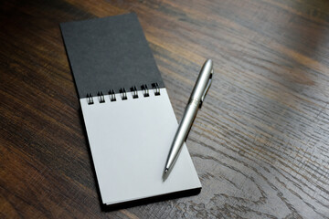 Silver pen and blank paper of notebook placed on wooden pattern desk at office for design ideas and taking notes.
