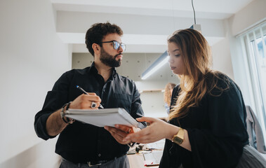 Two professional colleagues engaged in a serious discussion in a well-lit office environment, looking over important documents and strategizing.