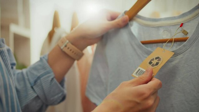 Fashion. A young woman of European appearance leisurely holds a tag with a logo in a stylish store. Slow motion modern woman, recycling sign on tag. Recycled clothing, sustainable clothing business