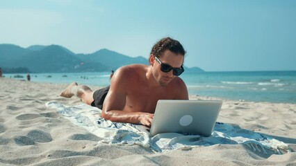 Freelancer professionally performs work using laptop on sandy beach. Guy work, despite surrounding beauty and seductive beach. Inspired by sea breeze, freelancer work hard combined with recreation.