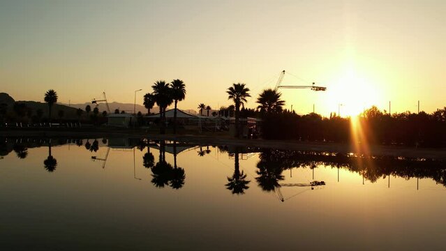 Sunrise in the wakepark. the drone rises up in the water the golden sunlight is beautifully reflected in the foreground a palm tree is growing no one has woken up yet. High quality 4k footage.