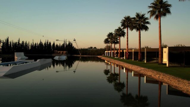 Sunrise in the wakepark. the drone rises in the water, the golden sunlight is beautifully reflected in the foreground, palm trees grow on the shore. while everyone is sleeping High quality 4k footage.