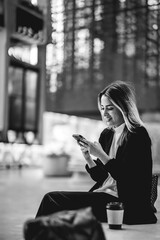Fototapeta premium Coffee break in a public city spot: beautiful and relaxed blonde latina executive sipping coffee and using the phone (in black and white)