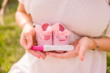 A pregnant woman holds her positive pregnancy test and pink baby shoes on her growing bump as a...