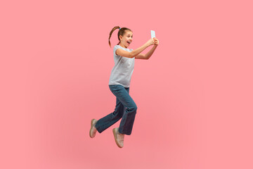 A young girl is captured mid-air, jumping energetically with a cell phone in hand. She appears joyful and carefree as she leaps into the sky with a mobile device.