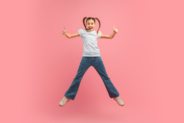 A young girl child is joyfully leaping into the air with her arms outstretched. She appears to be...