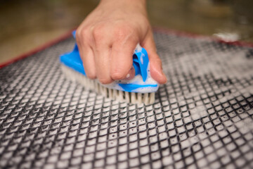 Using a brush, a person cleans a rug made of textile on the hardwood floor