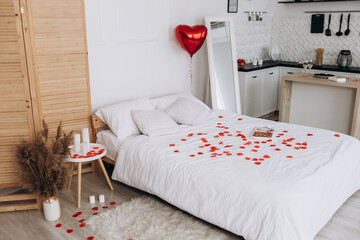 Bedroom and kitchen with many red flowers rose petals and candles in hotel room apartment. Valentine`s day concept celebration decoration for romantic evening. Love, holiday, party
