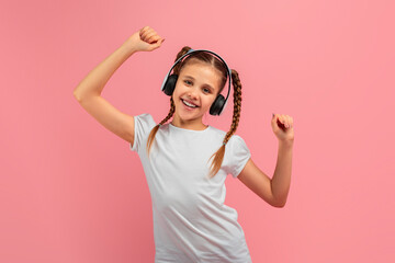 A young girl joyfully raises her arms while wearing headphones, showcasing a moment of triumph or...