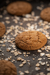 Craft and rustic four oatmeal cookies. Dark food aesthetics, black background with several oat flakes.