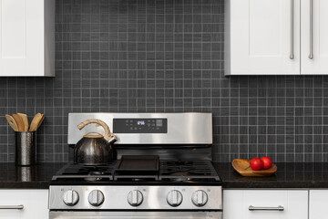 A kitchen detail with white cabinets, a black square tile backsplash, stainless steel stove, and...