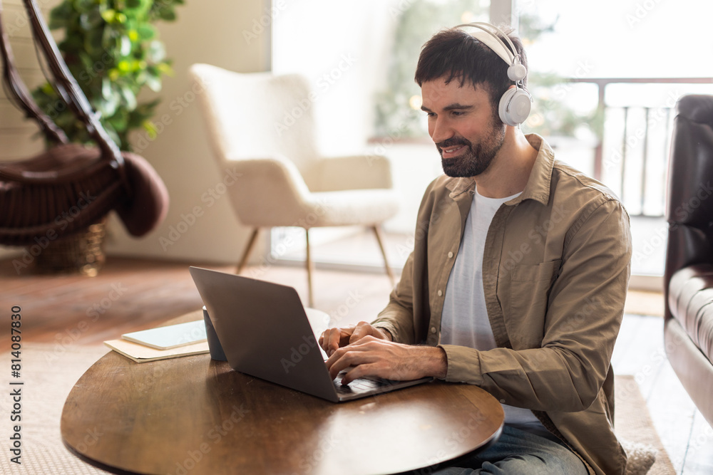 Poster a man is seated at a table, focused on his laptop screen, wearing headphones. he appears to be worki