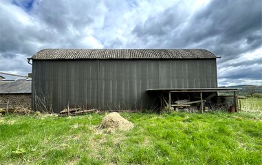 A large, industrial-looking metal barn, with a corrugated roof stands in the center of a green...