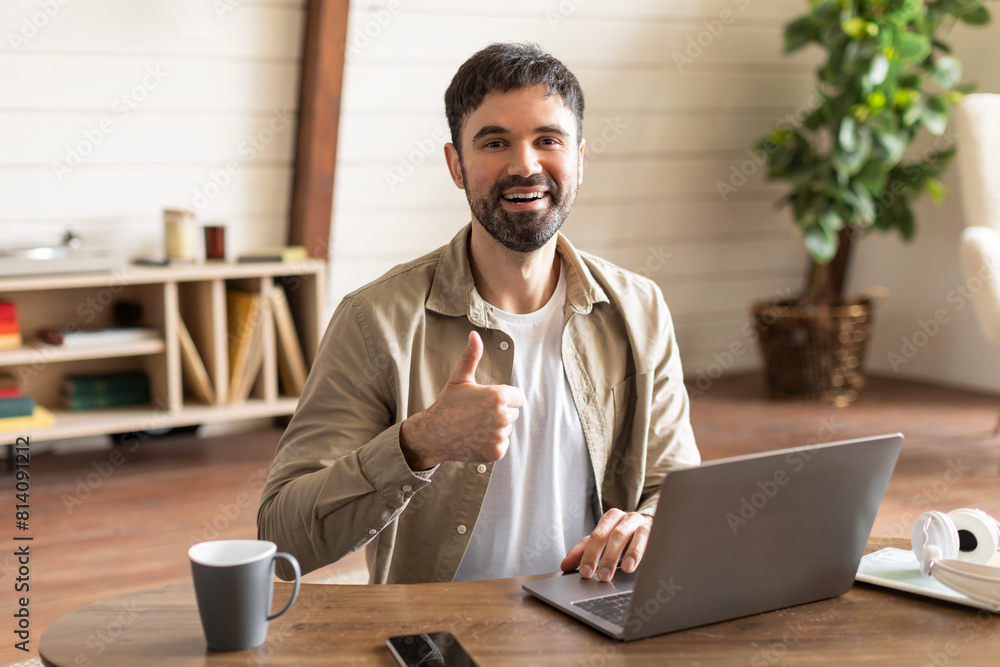 Fototapete a man is seated at a table with a laptop in front of him. he is smiling and extending his thumb up i