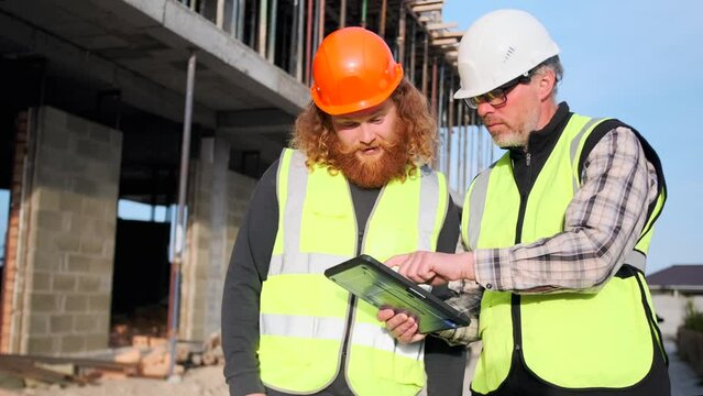 Team of two specialists use tablet computer on construction site inspection building project, civil engineer and worker looking blueprints plan on screen.