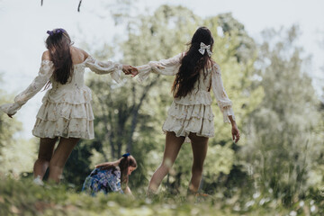 Three sisters run playfully through a lush park, hands linked, dressed in flowy dresses on a sunny,...