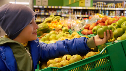 Close-up of a cute happy boy choosing a green apple in a supermarket