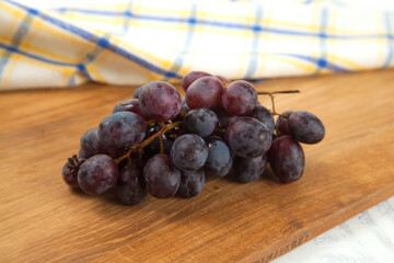 Cutting board with bunch of organic black grapes on white wooden background..
