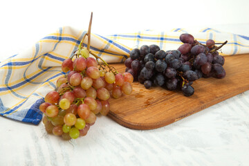 Cutting board with bunches of organic pink and dark blue grapes on white wooden background..