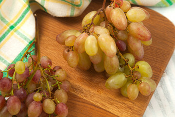 Close up view of bunch of organic pink grapes on wooden cutting board..