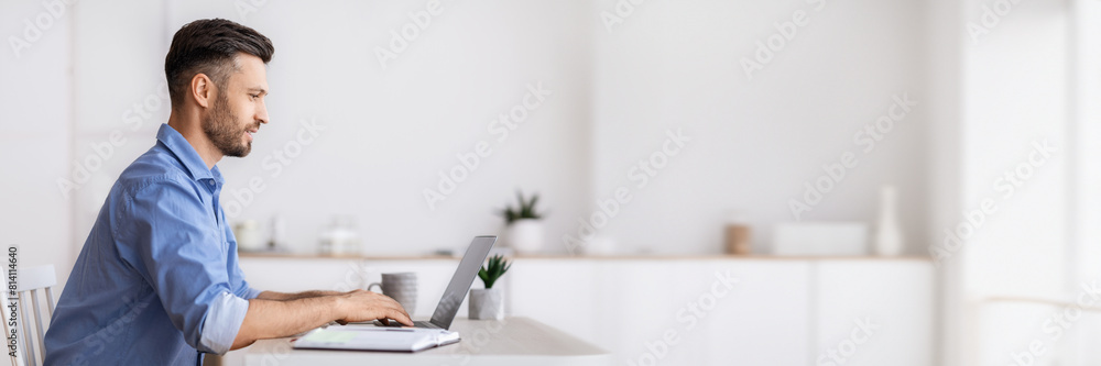 Poster handsome millennial businessman sitting at workplace in white office, working on laptop, typing on c