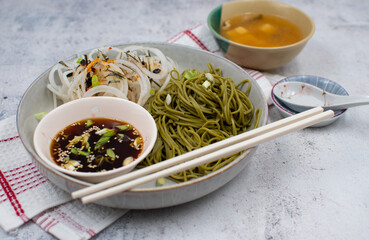 Vegan green tea noodles (matcha noodles)  and dipping sauce, daikon salad. White bowl, chopsticks, miso soup