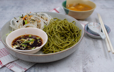 Vegan green tea noodles (matcha noodles)  and dipping sauce, daikon salad. White bowl, chopsticks, miso soup