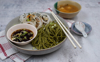 Vegan green tea noodles (matcha noodles)  and dipping sauce, daikon salad. White bowl, chopsticks, miso soup