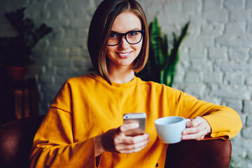 Portrait of successful young businesswoman with stylish haircut holding coffee cup in hand and...