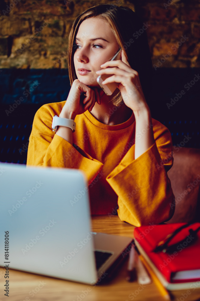 Aufkleber pondering young woman looking out of window and calling on telephone device while sitting at laptop 