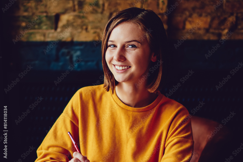 Poster portrait of successful student with short haircut smiling at camera while holding notepad for notes 
